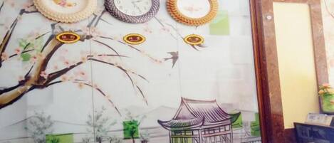A wall with a mural of a traditional building and trees, a clock, and three wall-mounted clocks.