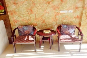 Dos sillas con cojines estampados y una pequeña mesa redonda con un libro, frente a una pared texturizada con un enchufe.