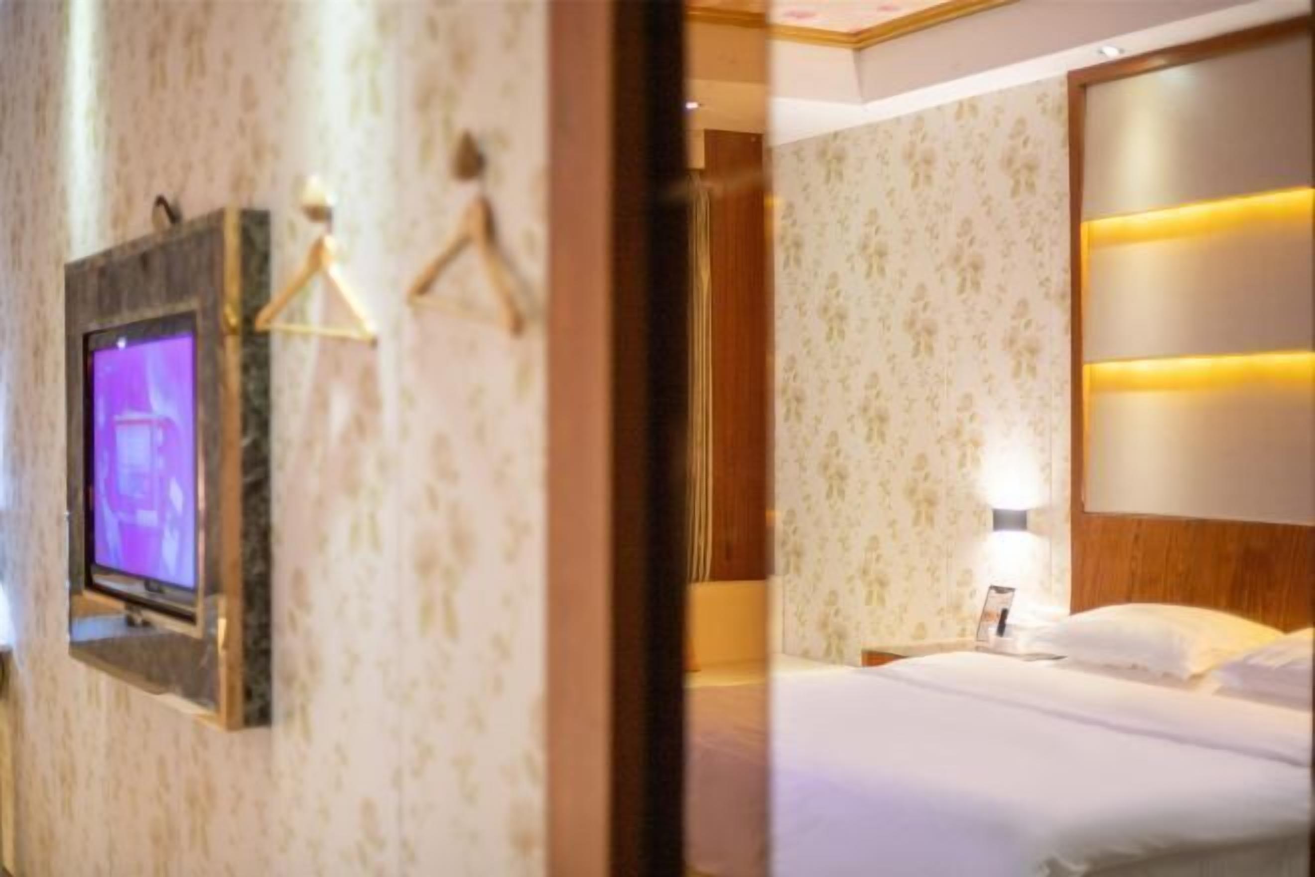 A hotel room with a bed, a television mounted on the wall, and a nightstand with a lamp.