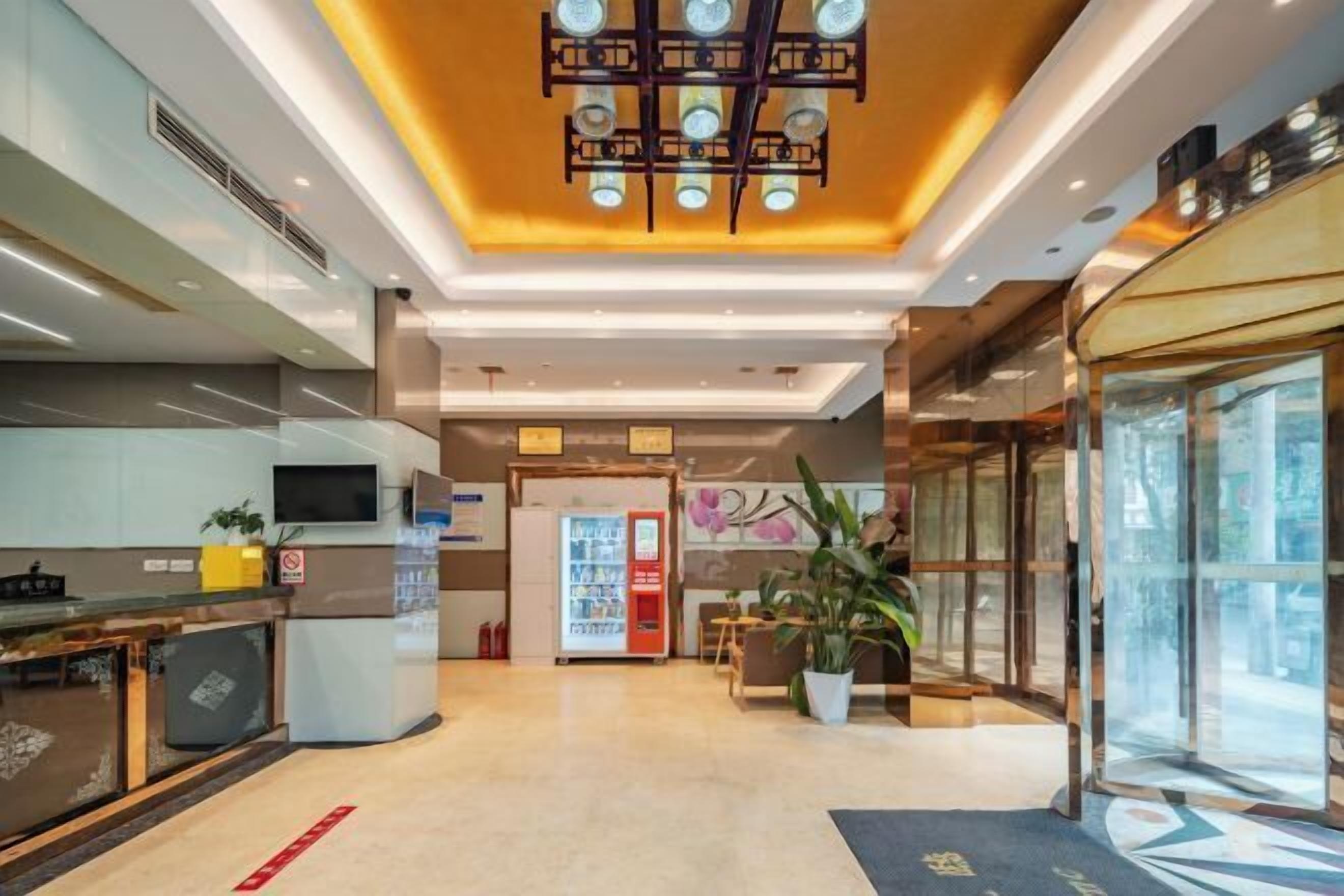 Un vestíbulo de hotel moderno con una recepción, máquinas expendedoras, una planta grande en maceta y una entrada de vidrio.
