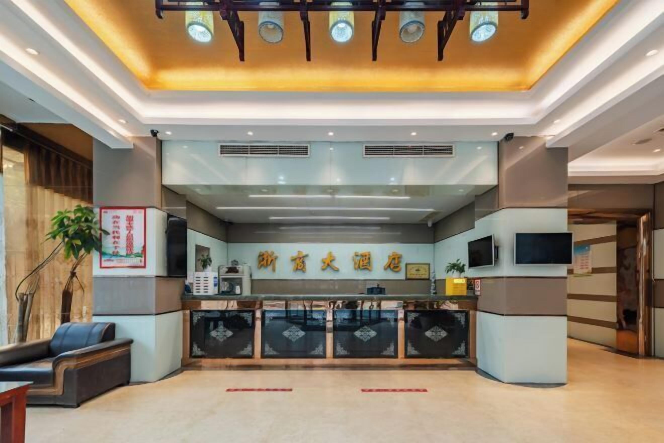 A hotel reception area with a modern design, featuring a reception desk, seating area, and a ceiling with recessed lighting.