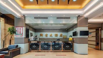 A hotel reception area with a modern design, featuring a reception desk, seating area, and a ceiling with recessed lighting.