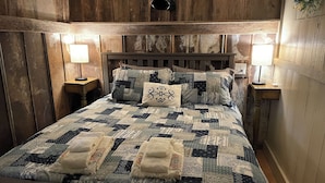Una cama con un colcha de retazos, dos lámparas de noche y un cabecero de madera.