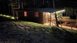 Una cabaña de madera pequeña con un porche, rodeada de árboles y un espacio cubierto de césped.