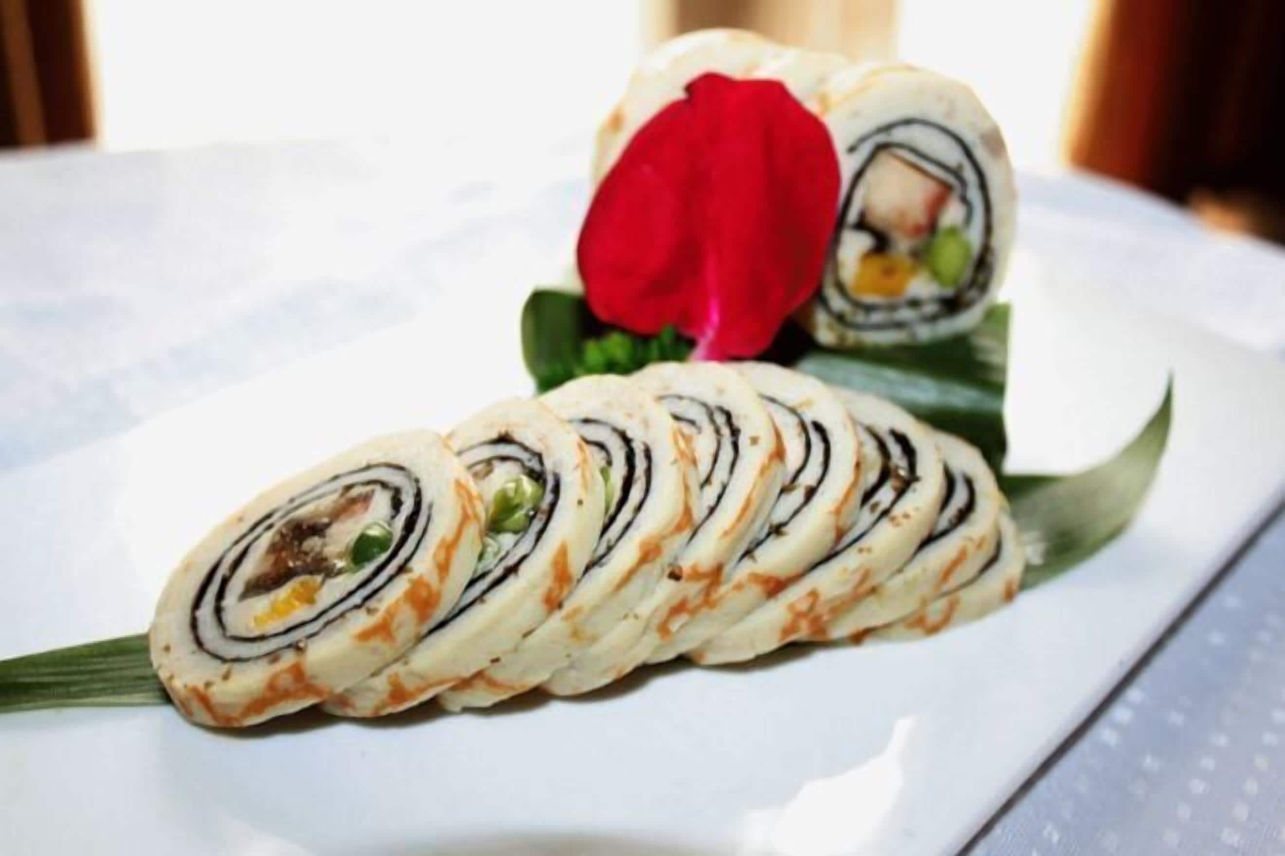 A plate with a rolled food item, possibly sushi, garnished with a red flower.