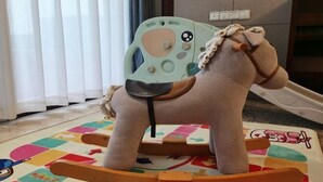 A rocking horse with a light blue seat and a brown saddle, placed on a colorful play mat.