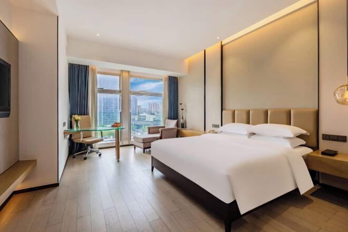A modern hotel room with a large bed, a desk, and a view of the city.