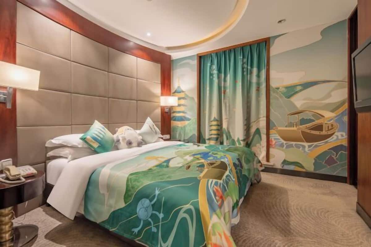 A hotel room with a large bed, a headboard, a bedside table with a lamp, a phone, and a wall with a mural.