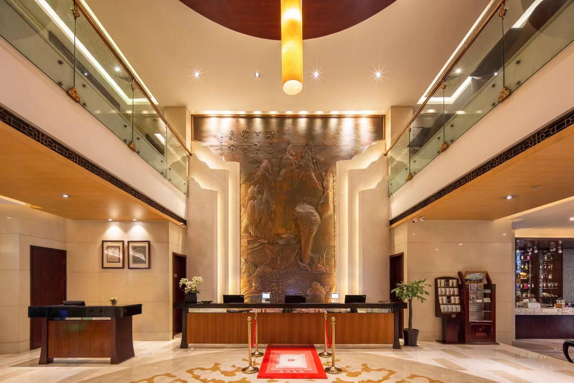 Un vestíbulo de hotel con una recepción, un mural grande en la pared y una escalera.