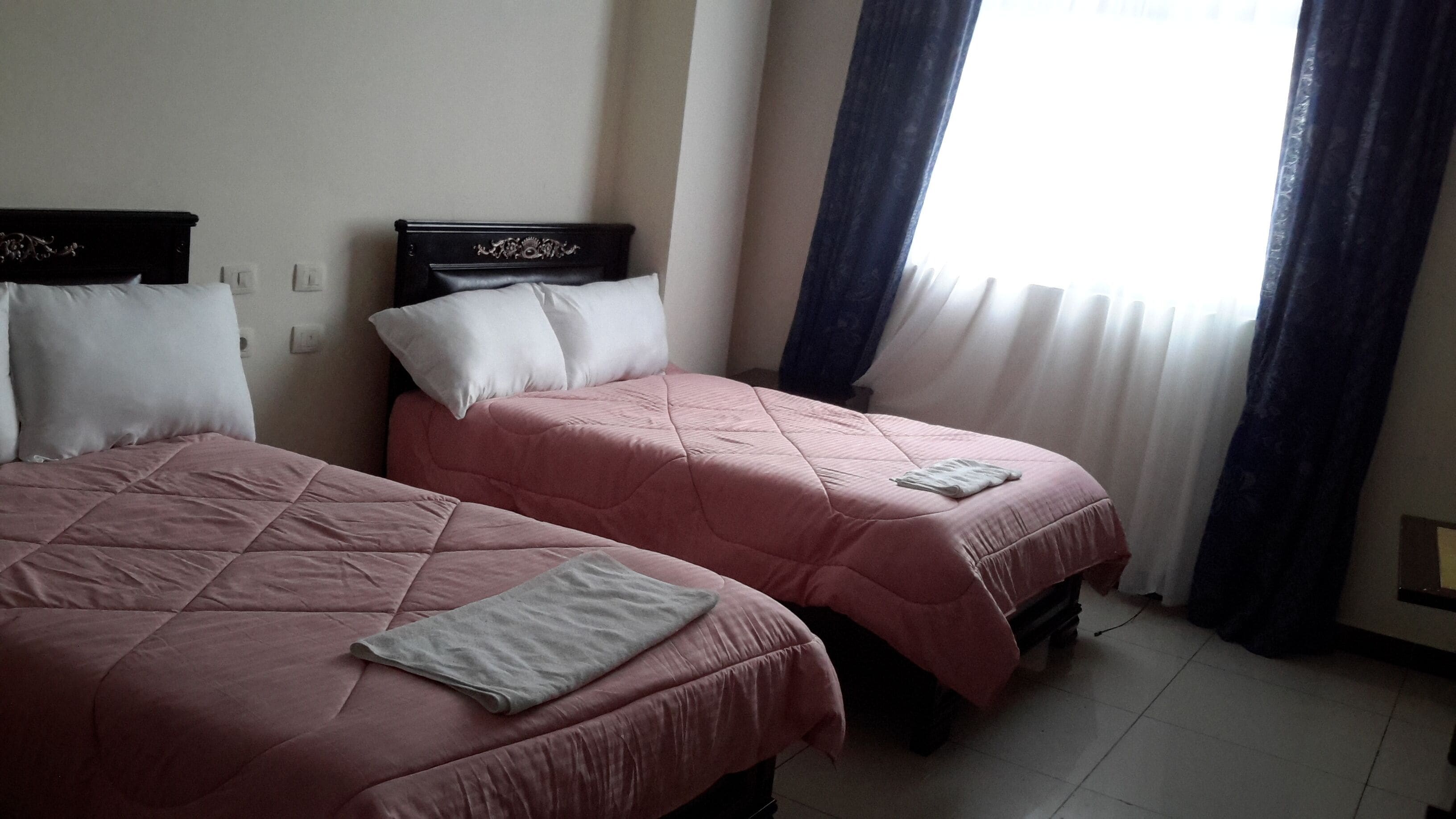 A hotel room with two beds, each with a headboard, and a window with curtains.
