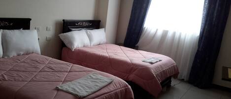 A hotel room with two beds, each with a headboard, and a window with curtains.