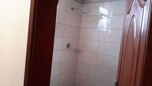 Une petite salle de douche carrelée, équipée d’une pomme de douche et d’un robinet.