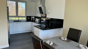 A modern kitchen with white cabinets, black countertops, and a central island. There is a dining table with chairs in the foreground.
