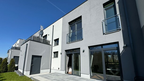A modern two-story residential building with large windows, a flat roof, and a paved driveway.