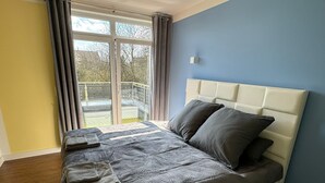 A bedroom with a large window, a bed with a headboard, and a view of a balcony.