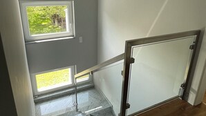 A staircase with a glass railing leading to a landing with a window overlooking greenery. - Vacation home near Katowice  (Bytom)