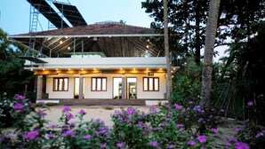 A modern house with a covered porch, surrounded by lush greenery and purple flowers. - Dolphin turf  - Beach front cottage, relaxing on the wide white sandy beach  (Cherthala)