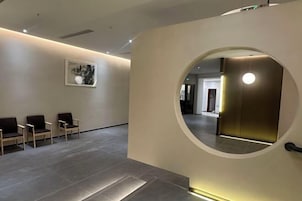 Un vestíbulo moderno con un espejo circular, un mostrador de recepción y una zona de estar con sillones.