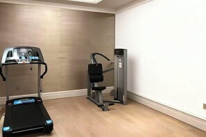 A room with a treadmill, a weight machine, and a wall-mounted TV.
