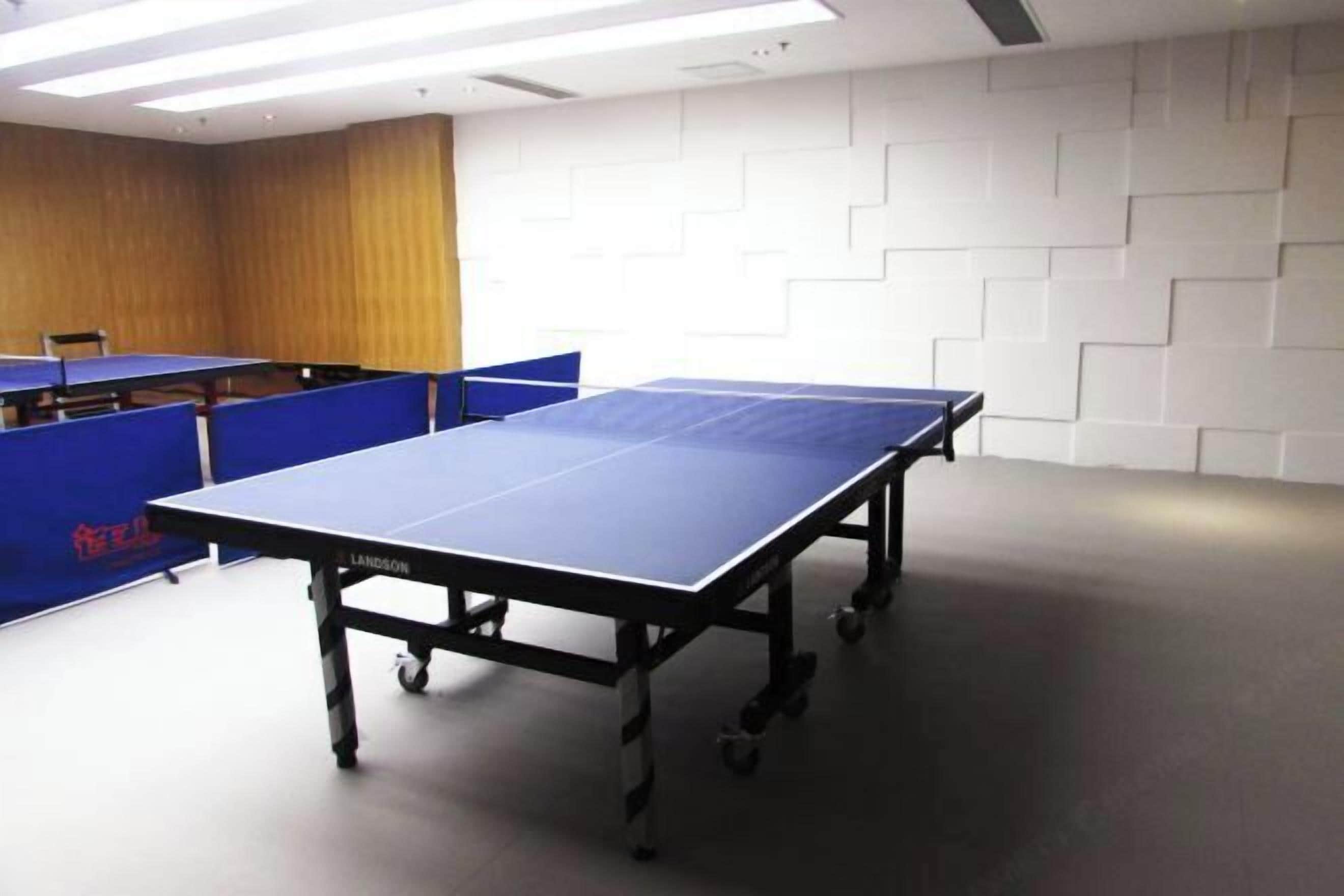 A ping pong table in a room with a white brick wall and a wooden panel on one side.