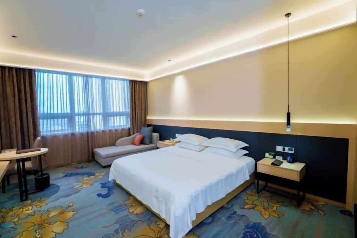 A hotel room with a large bed, a desk, a chair, a small table, and a window with curtains.