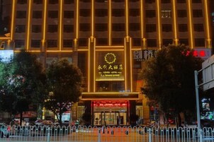Un hotel con un letrero llamativo, una entrada cercada y una calle bordeada de árboles.