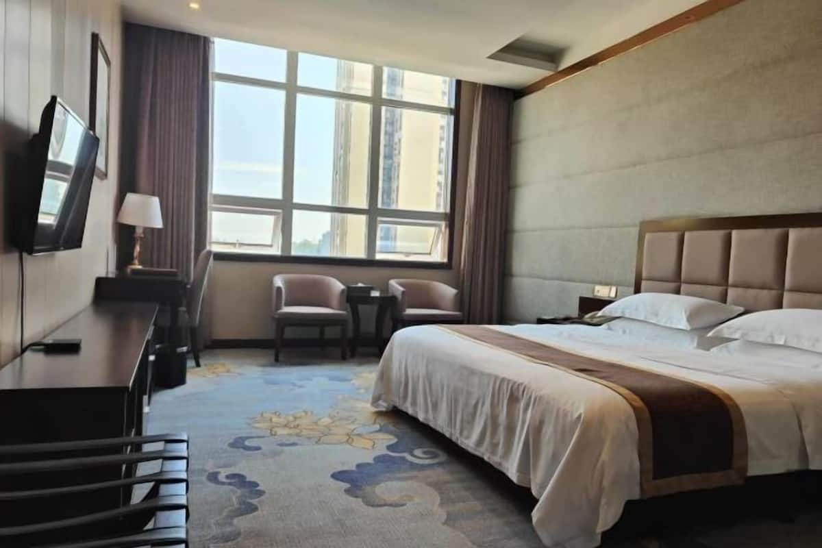 A hotel room with a large bed, a desk with a chair, a TV, and a window with curtains.