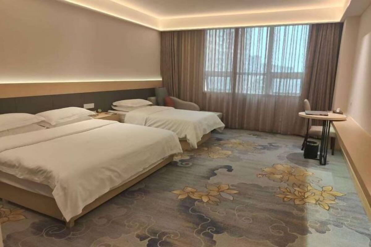 A hotel room with two beds, a small table, a chair, and a large window with curtains.