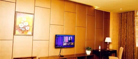 Habitación de hotel con televisor de pantalla plana montado en la pared, una mesita con lámpara, una silla y un banco con espacio para vinos.