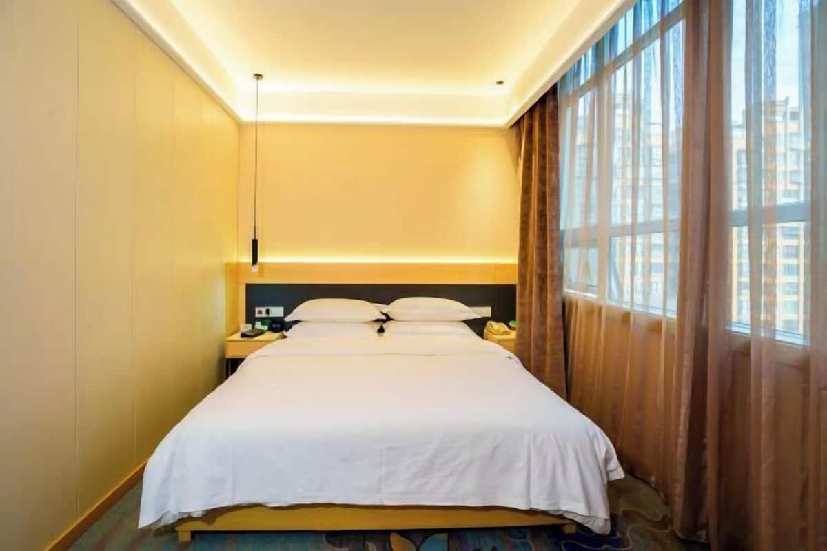 A hotel room with a large bed, bedside tables, a nightstand, and a window with curtains.