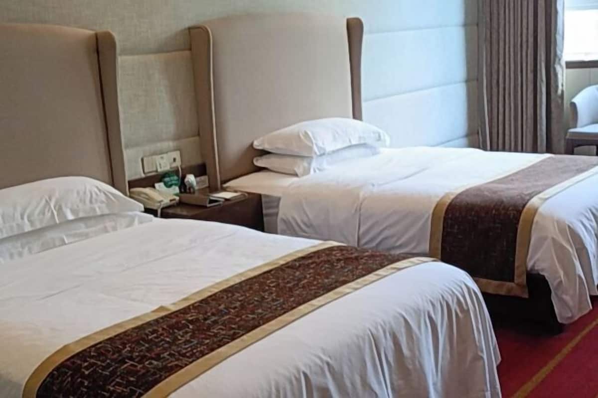 A hotel room with two beds, a red carpet, and a nightstand with a phone and a lamp.