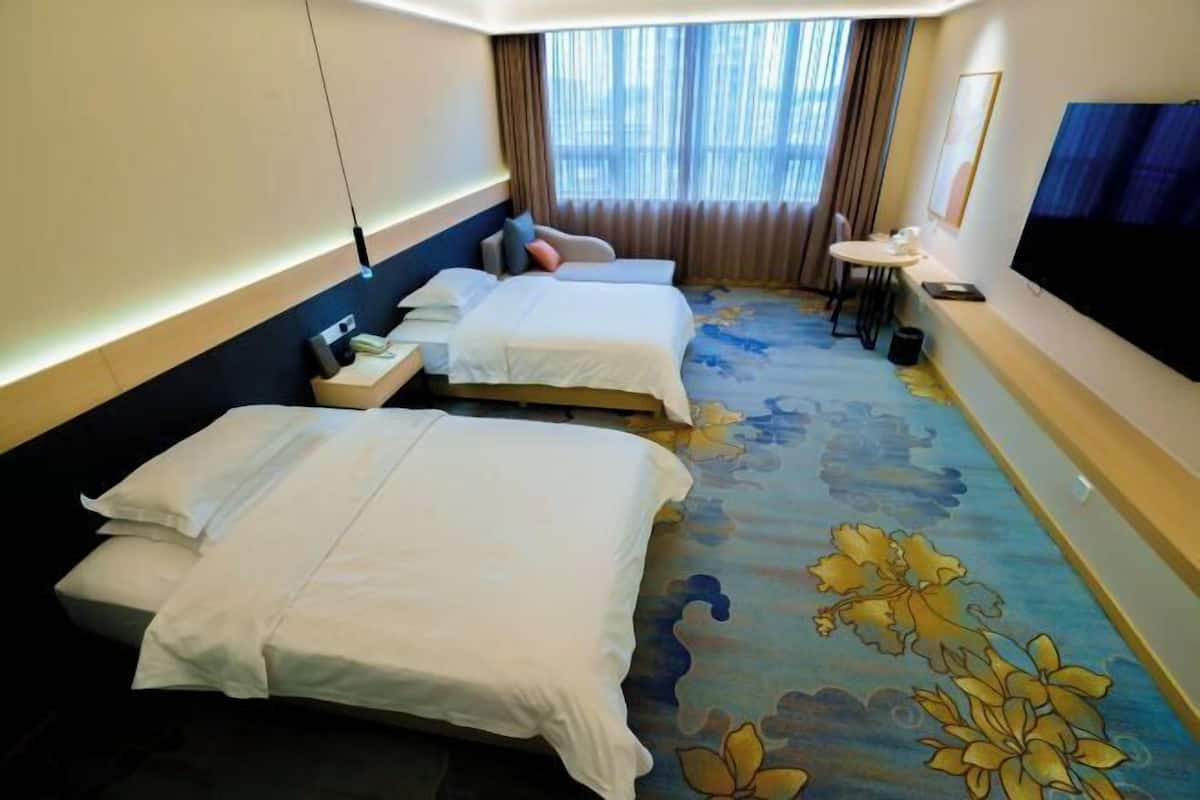 A hotel room with two beds, a TV, a small table, and a window with curtains.