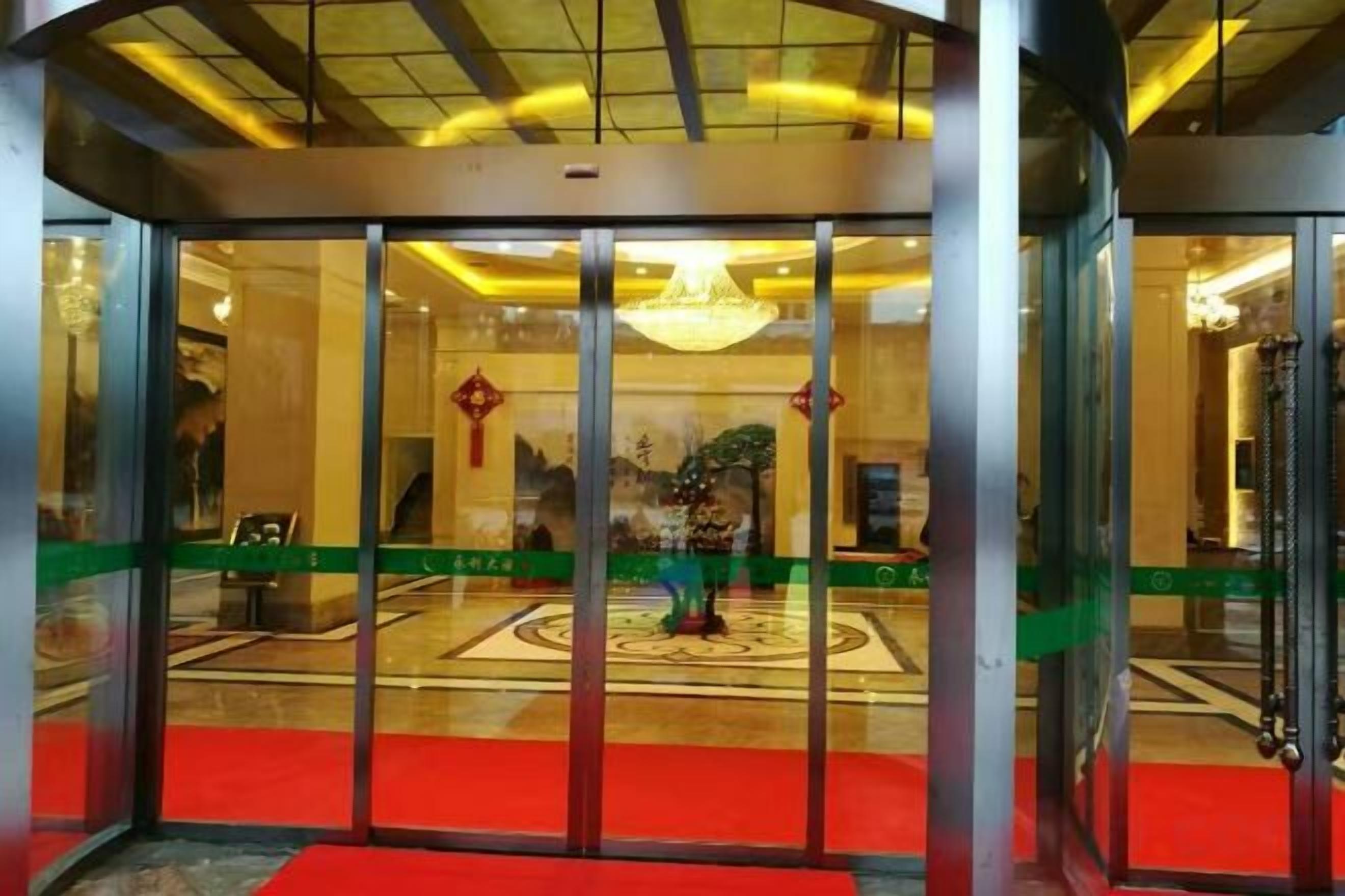 A revolving door leading into a lobby with a red carpet, a chandelier, and a patterned floor.