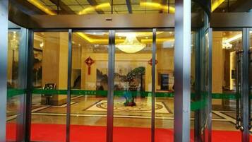 A revolving door leading into a lobby with a red carpet, a chandelier, and a patterned floor.