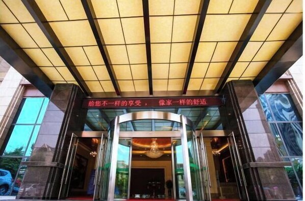 Una entrada de hotel con diseño moderno, que presenta fachada de vidrio y una entrada destacada con alfombra roja.