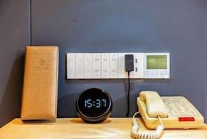 A desk with a digital clock displaying 15:37, a telephone, a power strip with multiple plugs, and a wall-mounted control panel. - Yongli Hotel (Yuechi)