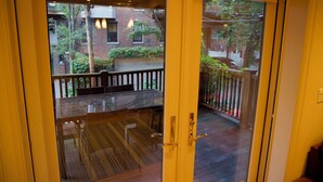A view through a glass door to a wooden deck with a table and chairs, a brick building, and a car in the background.
