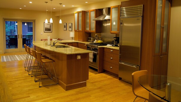 A modern kitchen with wooden cabinets, stainless steel appliances, and a glass dining table.