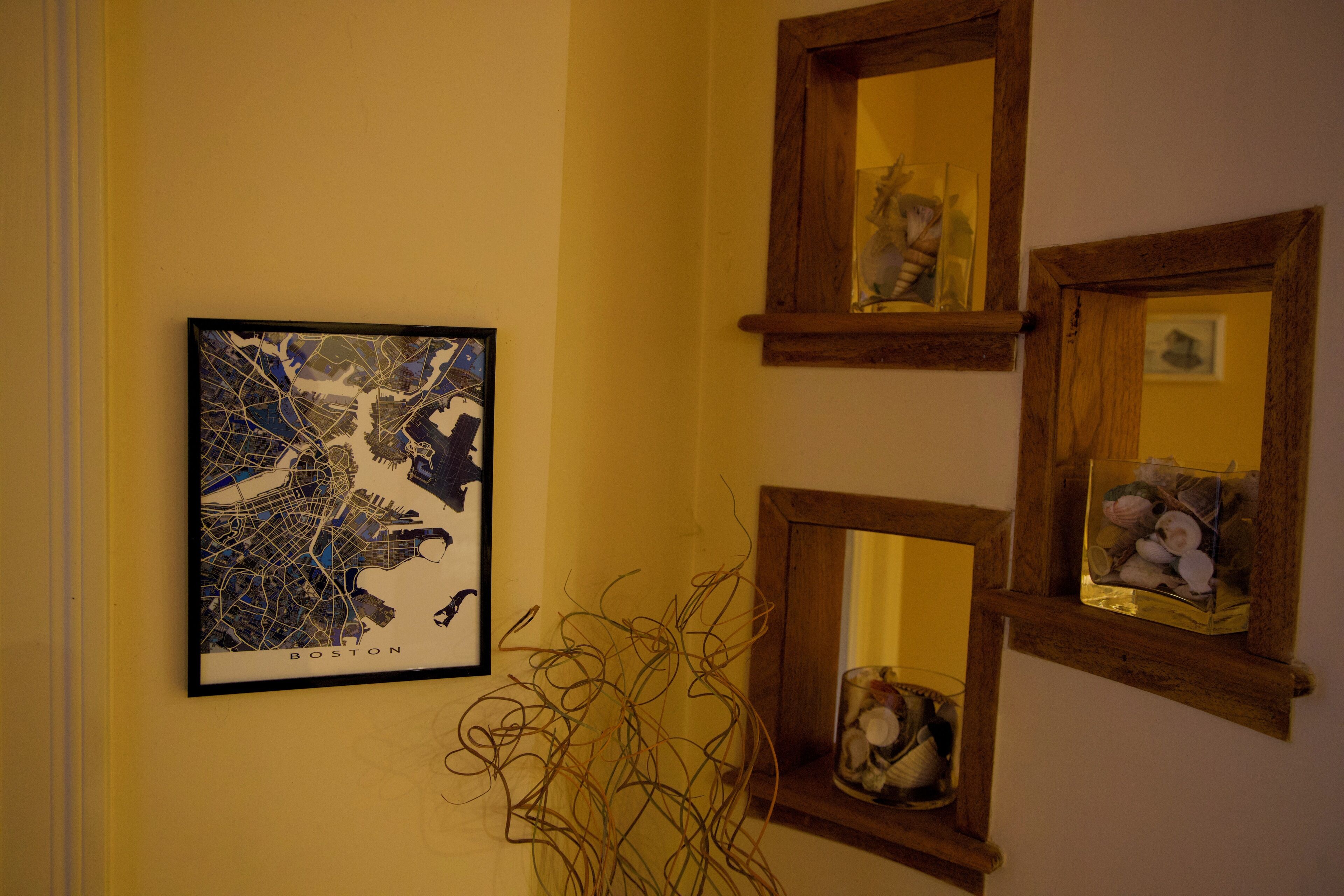 A framed map of Boston, a mirror with a sculpture, and a vase with seashells.