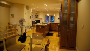 A modern kitchen with wooden cabinets, a dining area with a glass table, and a view of the outdoors.