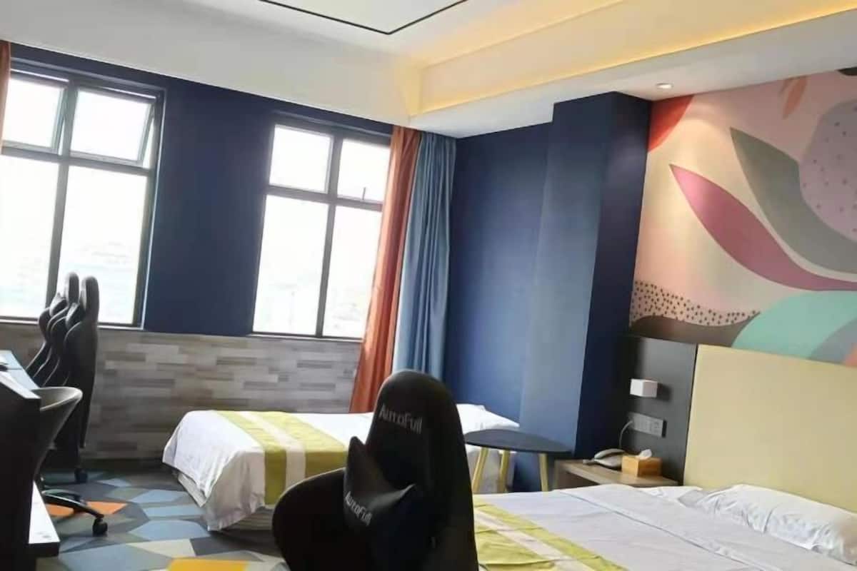 A hotel room with two beds, a desk, a chair, and a large window.