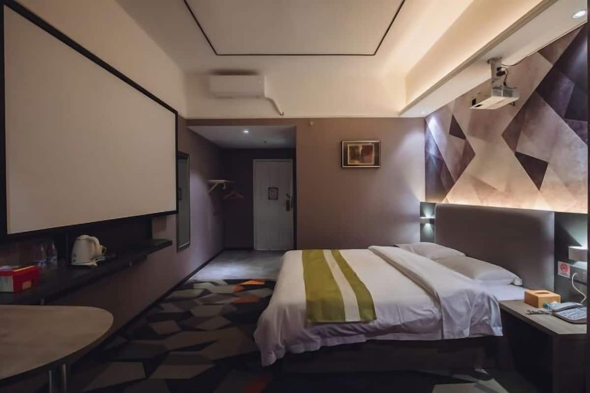 A hotel room with a bed, bedside table, lamp, and a view of the hallway.