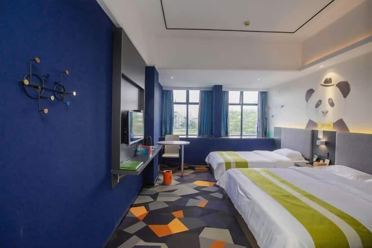 A hotel room with two beds, a desk, a chair, a TV, and a large window with curtains.