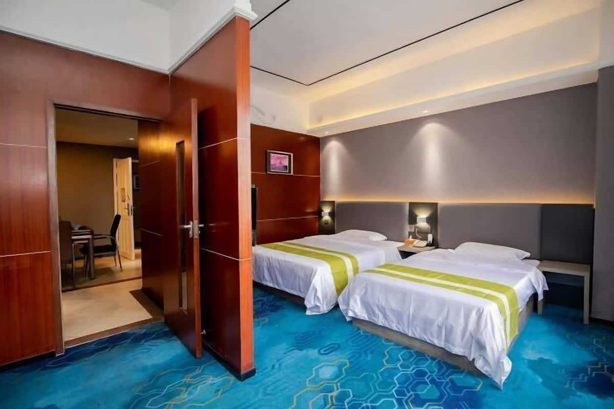 A hotel room with two beds, a wooden wardrobe, a desk with a chair, and a bathroom visible through an open door.