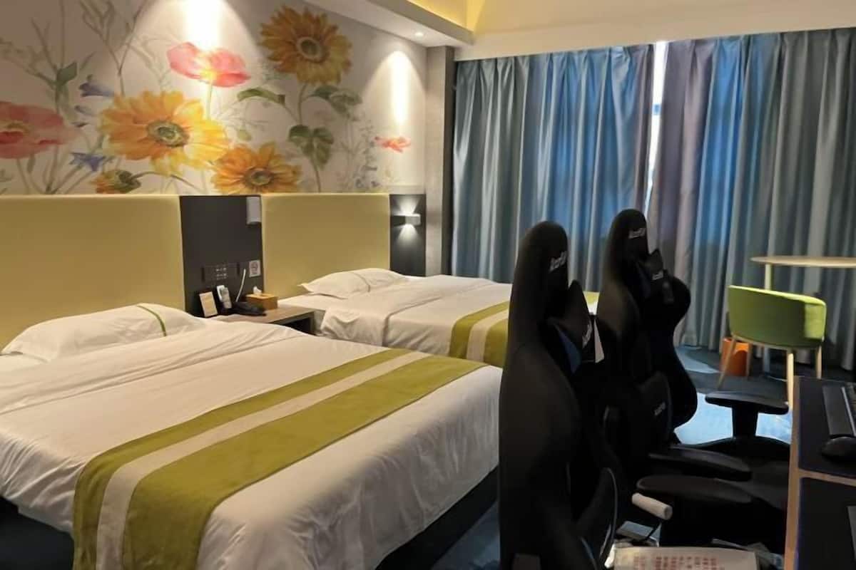 A hotel room with two beds, a desk with a computer, and a gaming chair.
