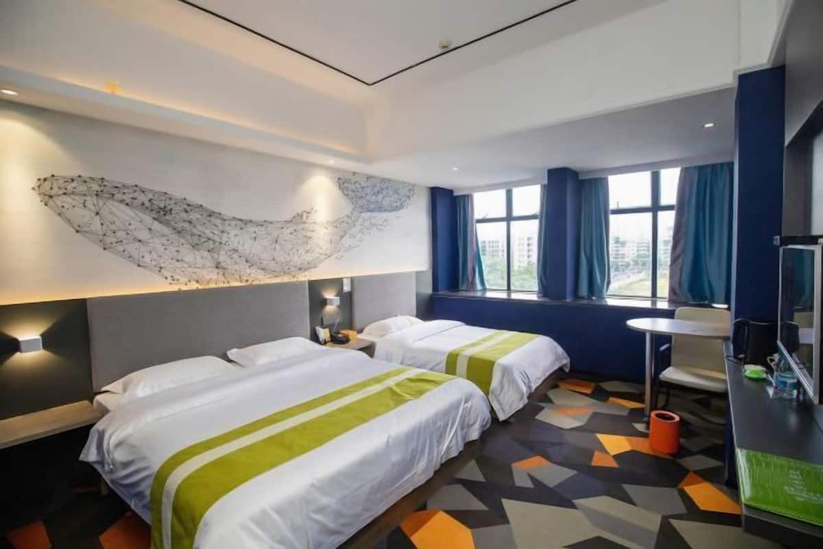 A hotel room with two beds, a large abstract wall art piece, a window with curtains, and a desk with a chair.