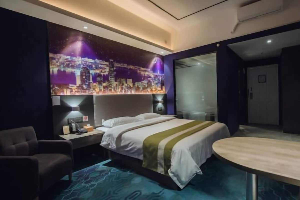 A hotel room with a bed, bedside table, lamp, chair, and a round table.
