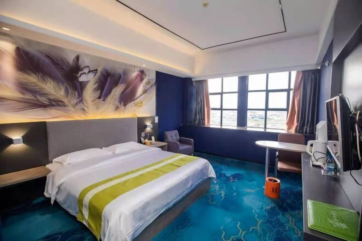 A hotel room with a bed, a desk, a chair, a large window, and a wall mural.