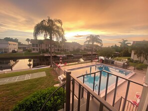 Ein Swimmingpool mit Blick auf einen Sonnenuntergang, ein Tennisplatz und ein Grill.