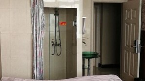 Ένα δωμάτιο ξενοδοχείου με ένα κρεβάτι, μια περιοχή με ντους που διαχωρίζεται με μια γυάλινη πόρτα και έναν πράσινο νιπτήρα.
